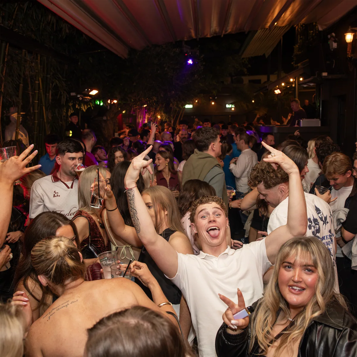 A packed T. Morris garden with guests smiling, dancing and raising their hands towards the camera.