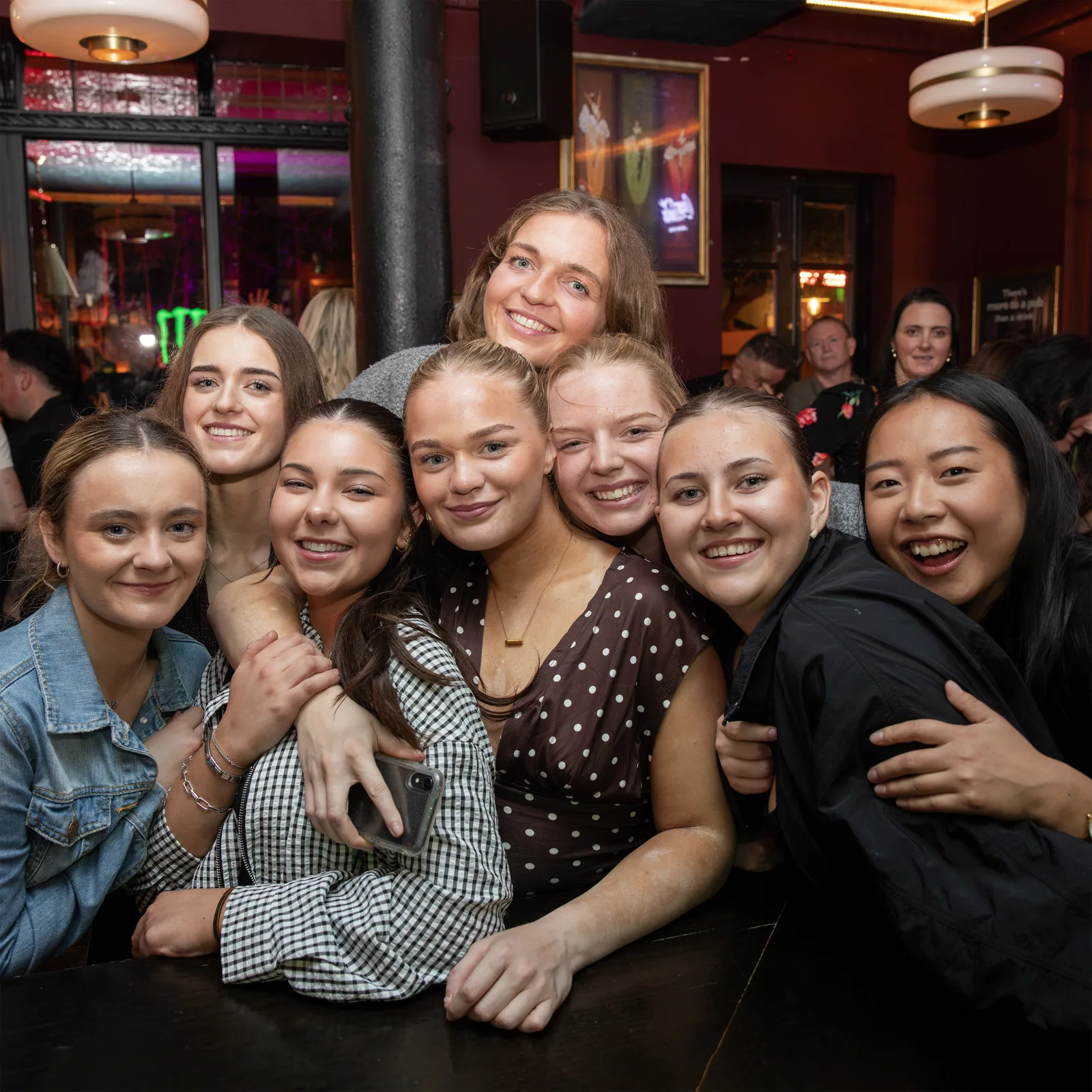A group of friends gathered together in the bar, smiling at the camera.